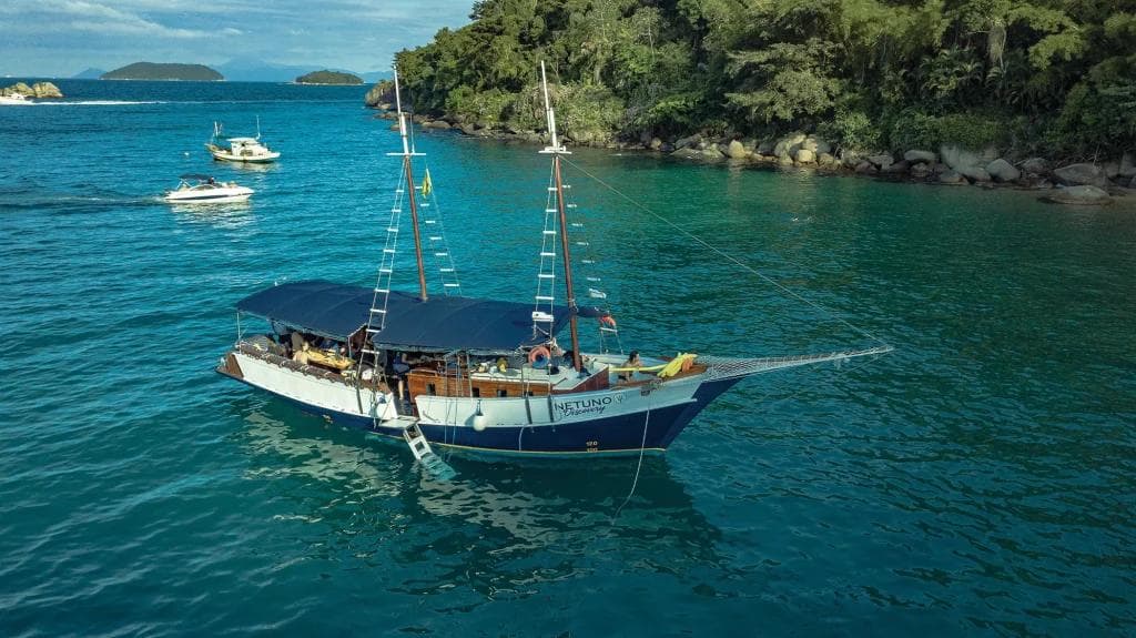 Barco turístico ‘Netuno Discovery’ navegando em águas tranquilas próximas a costa florestal de Balneário Camboriú