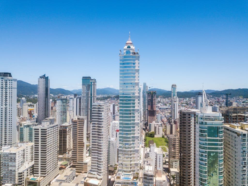 Edifício Millennium Palace em Balneário Camboriú com pináculo clássico, fachada de vidro azulado e frisos claros em cada andar
