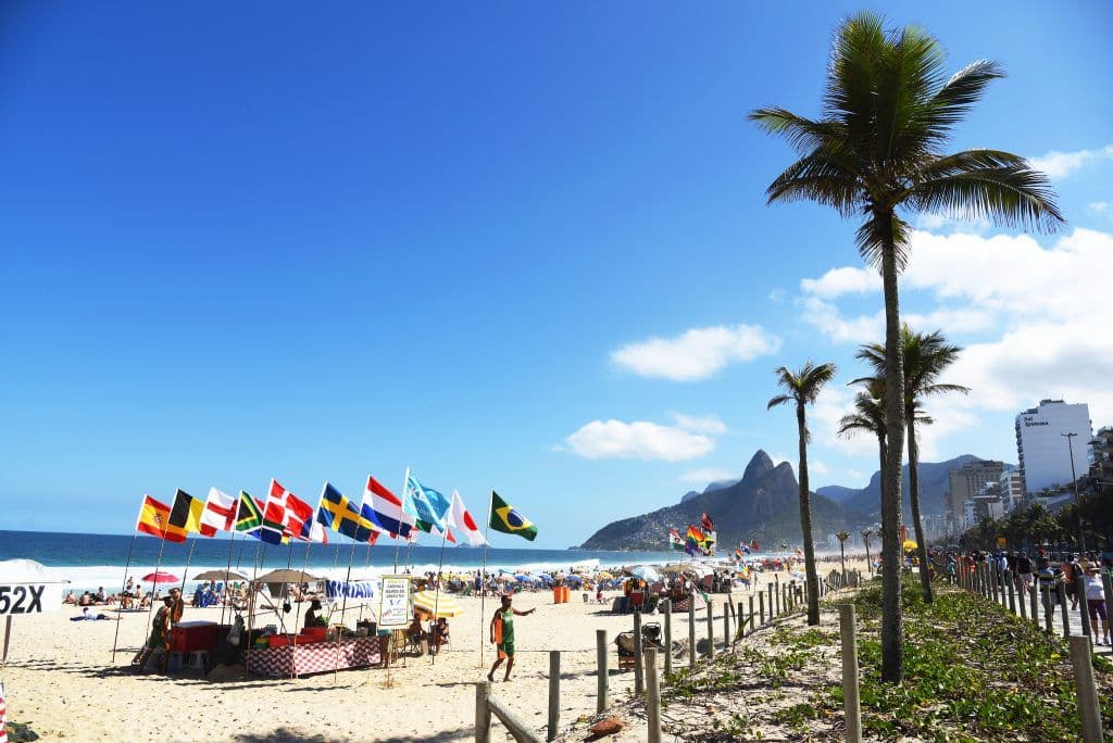 Orla da Praia de Ipanema no Rio de Janeiro (RJ) com bandeiras de vários países, palmeiras e o Morro Dois Irmãos ao fundo