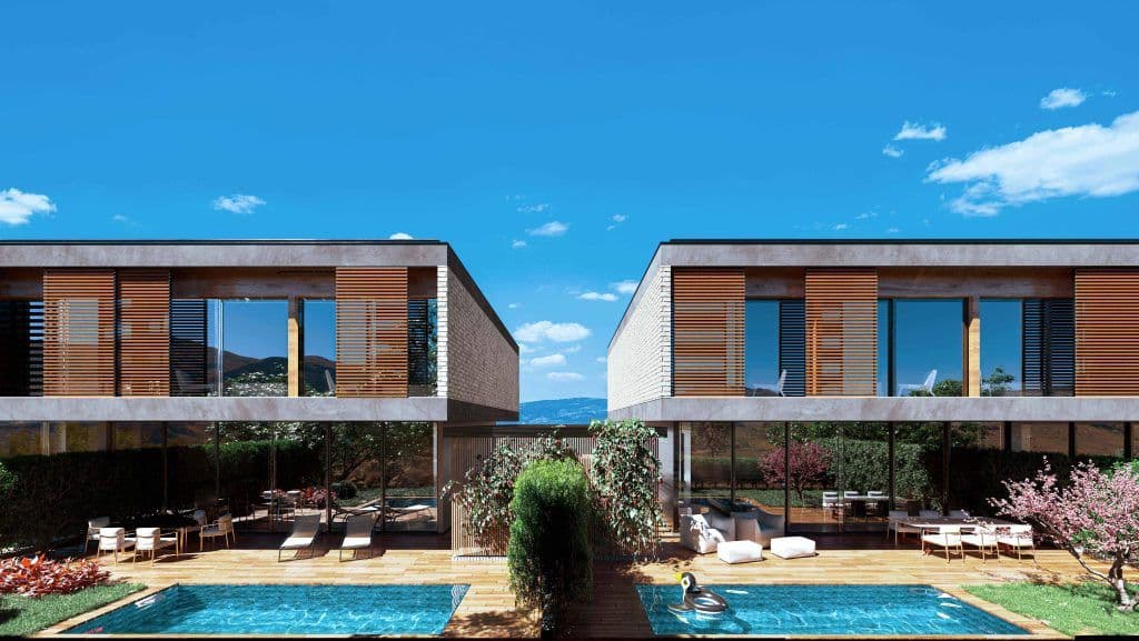 Duas casas modernas em concreto e madeira, unidas por deck com piscina, rodeadas por vegetação e montanhas ao fundo.